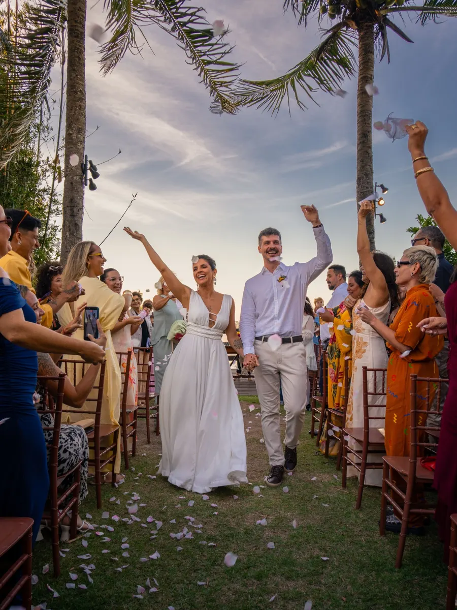 A bride and groom walk back down the aisle under palm trees as their guests throw petals