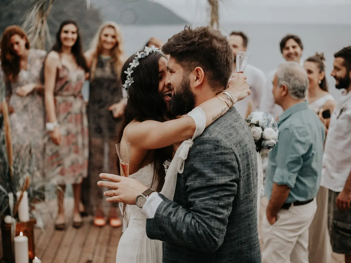 A couple hug on a terrace above the sea, surrounded by their friends